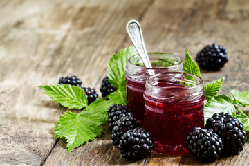Two jars of blackberry jam, fresh berries and green leaves in an