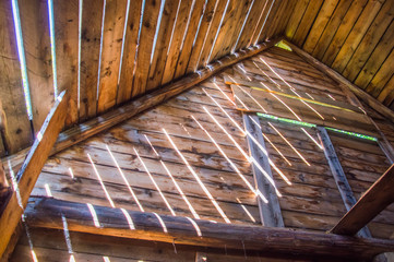 свет падает через щели между досок на крыше в деревянном доме