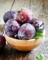 Large purple plum with water drops and leaves in a wooden bowl,