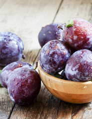 Large purple plum with water drops and leaves in a wooden bowl,