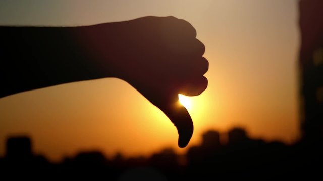 Female hand showing a thumb down gesture at city sunset