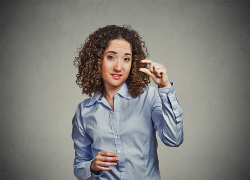 skeptical young woman showing small amount gesture with hand fingers