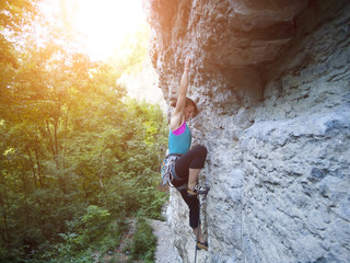 Young woman with rope climbs on the rock.