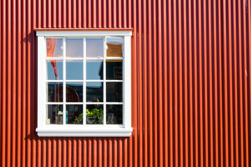 Red wall made of corrugated iron and a white window