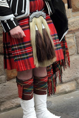 Scottish bagpiper dressed in kilt playing bag pipes, lower part with tartan skirt