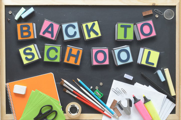 Some cube letters composing the words BACK TO SCHOOL on a blackboard. Some school materials representing the start of a new educational course.