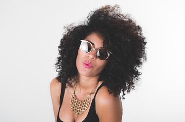 Headshot hispanic model wearing black dress, golden necklace, sunglasses and curly hair making kiss lips for camera