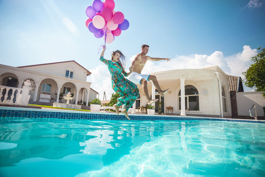 Happy young couple jumping into the pool while holding a bunch of balloons  - Powered by Adobe