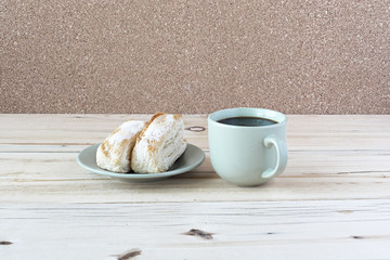 A pair of flaky biscuits with cup of tea on a wooden surface