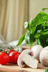 Food ingredients for pizza or pasta dishes on a wooden table in the rustic kitchen. Fresh cherry tomatoes, mushrooms, basil leaves. Closeup. Copy space. Free space for text