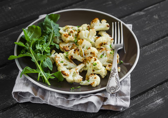 roasted cauliflower and fresh arugula on a brown plate on a dark wooden background