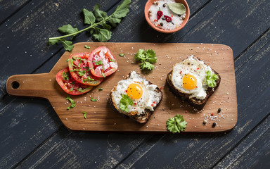 Fototapeta na wymiar toast with feta cheese and fried quail egg, fresh tomatoes on a dark wooden surface - a healthy Breakfast or snack