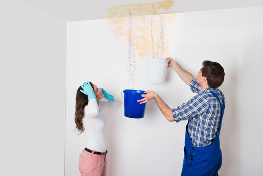Woman With Worker Collecting Water From Ceiling In Bucket