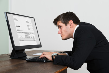 Businessman Looking At Invoice On Computer