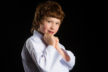 Smiling karate boy in white kimono isolated on black background