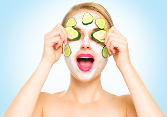 Funny spa woman applying fresh facial mask with cucumbers