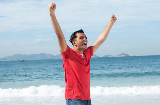 Jubelnder Latino im roten Shirt am Strand