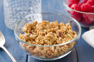 granola in white bowl with milk and fruits on white wooden background
