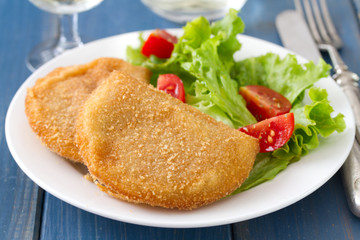 portuguese meat cookies with fresh salad on white dish on blue background