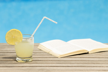 Glass of iced lemonade and opened book on the table - poolside
