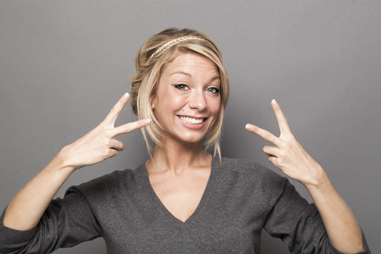 satisfaction concept - excited young woman with trendy blonde hair making the sign of victory twice for agreement