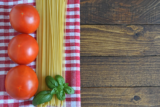 Spaghetti, fresh tomatoes and basil leaves on the wooden background