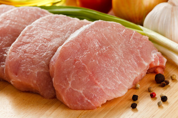 Raw pork chops on cutting board and vegetables 