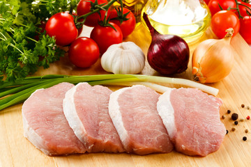 Raw pork chops on cutting board and vegetables 
