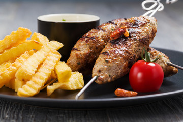 Barbecued kofta - kebeb with fries and vegetables on a plate.