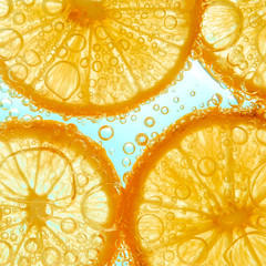 Fresh orange slice in water with bubbles on sky background