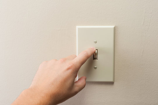 Hand turning wall light switch off. color image in horizontal orientation