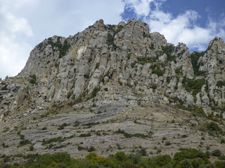 High mountain with green vegetation and white cumulus clouds in the blue sky 