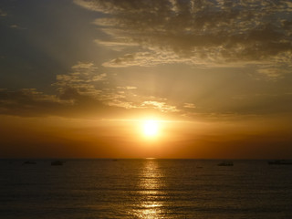 Naklejka na ściany i meble Sunrise over the sea, brilliant water, grey sky and clouds in orange sunshine. Sunlight path.