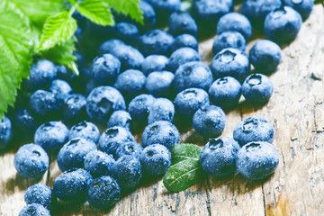 Fresh blueberries and green leaves on the old wooden background,