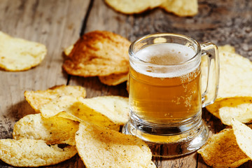 Light beer and chips on the old wooden background, selective foc