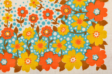 Floral pattern on fabric. Yellow and orange flowers with blue dots print as background.