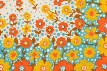 Floral pattern on fabric. Yellow and orange flowers with blue dots print as background.