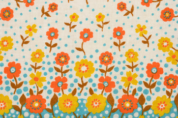 Floral pattern on fabric. Yellow and orange flowers with blue dots print as background.