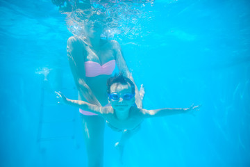 Young mother and toddler son swimming underwater in pool and having fun