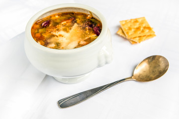 Bowl of minestrone soup with grated parmesan and crackers on white background