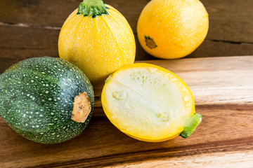 Raw round yellow and green zucchini and a cut one on a wooden background
