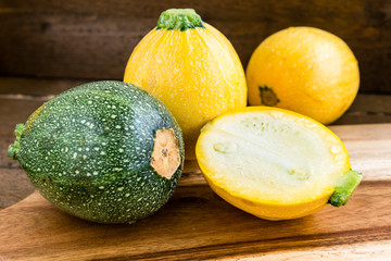 Raw round yellow and green zucchini and a cut one on a wooden background