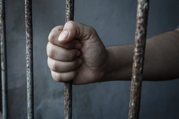 hands of jail holding prison bars
