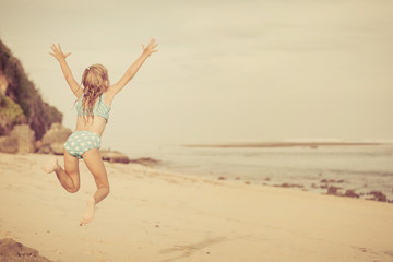 Little girl  jumping on the beach at blue sea shore in summer va