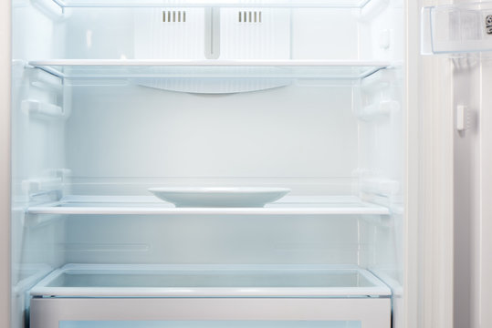 Empty white plate in open empty refrigerator. Weight loss diet concept.