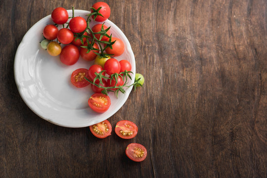 Multicolored cherry tomatoes in white plate on a wooden background, of vegetarian food, vegetables