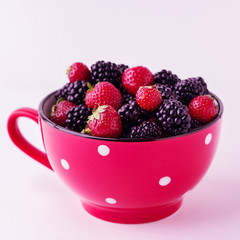 Blackberries and strawberries in a red plate. Isolated backgroun