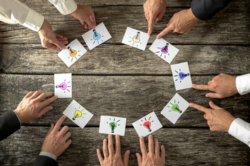 Teamwork and brainstorming concept with businessmen seated around a table each pointing to cards...