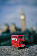 A toy British double decker bus with the Houses of Parliament out of focus in the background