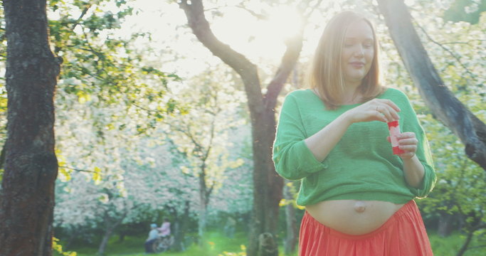 Merry Pregnant Woman among Blooming Trees